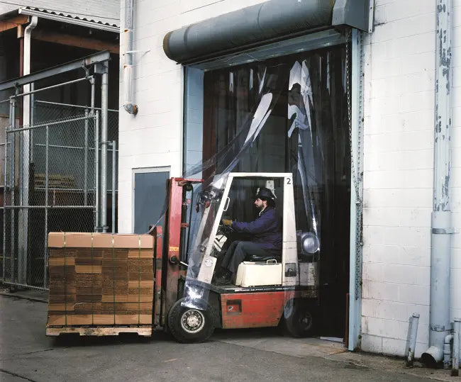 Clear PVC strip curtain installed in an industrial warehouse doorway, providing visibility, airflow control, and separation between interior work areas.